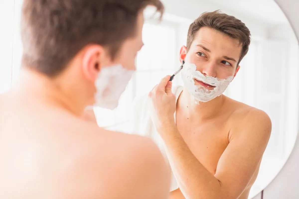 Hombre afeitándose frente al espejo con espuma blanca en la cara
