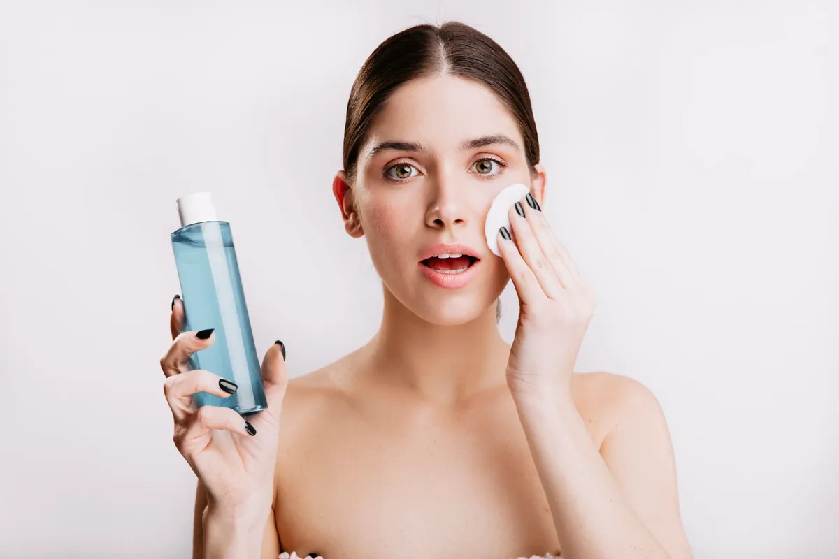 Mujer limpiándose la cara con agua micelar y un disco de algodón