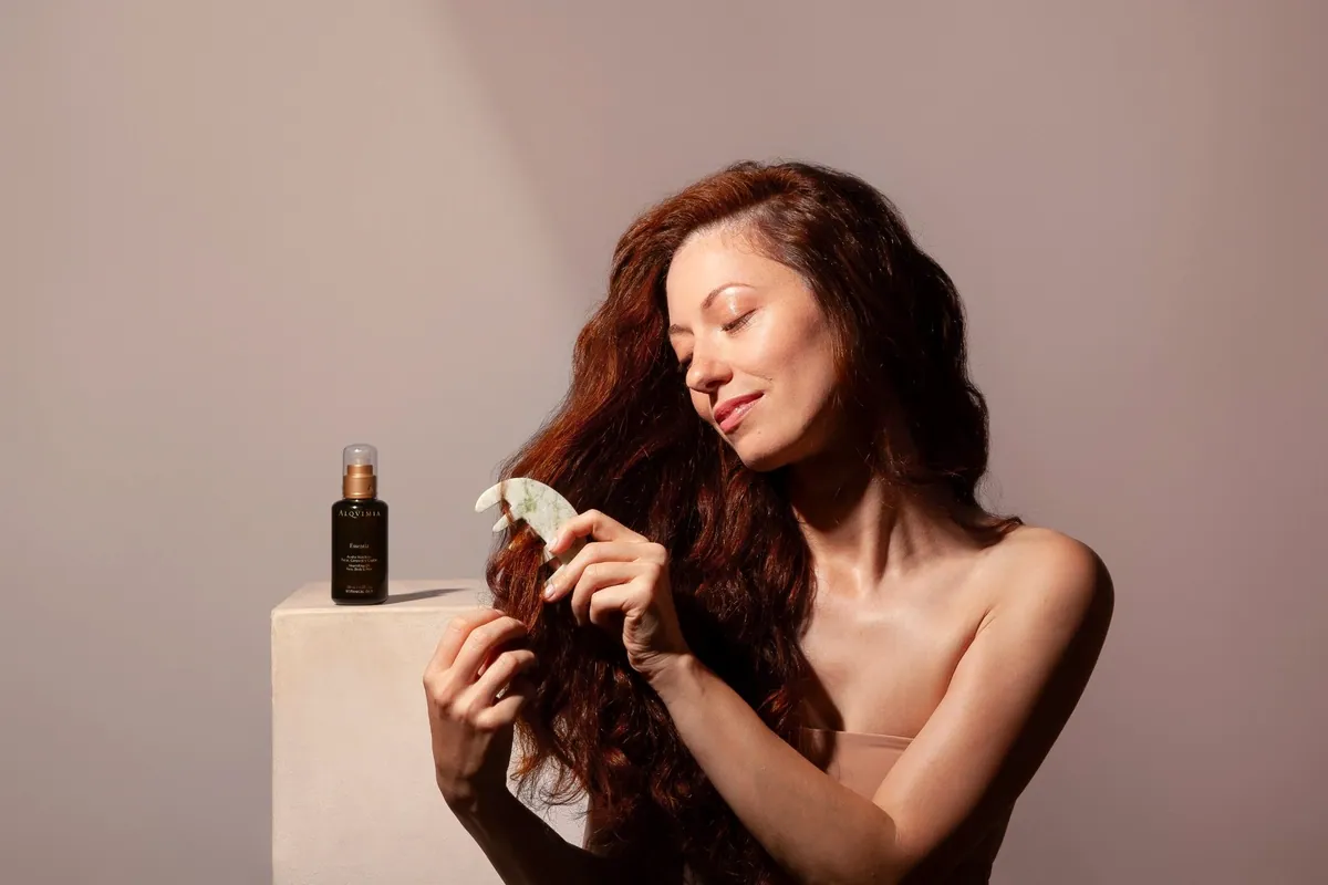 Mujer aplicándose el aceite Essentia en el pelo con una piedra de gua sha
