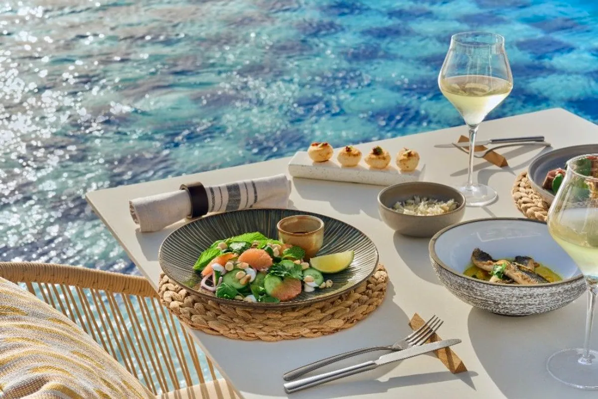 Mesa junto a la piscina con ensalada, panecillos de queso y copas de vino blanco