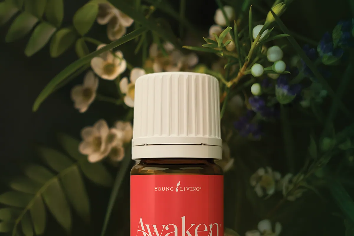 Frasco rojo de Awaken de Young Living de 5 ml entre hojas y flores