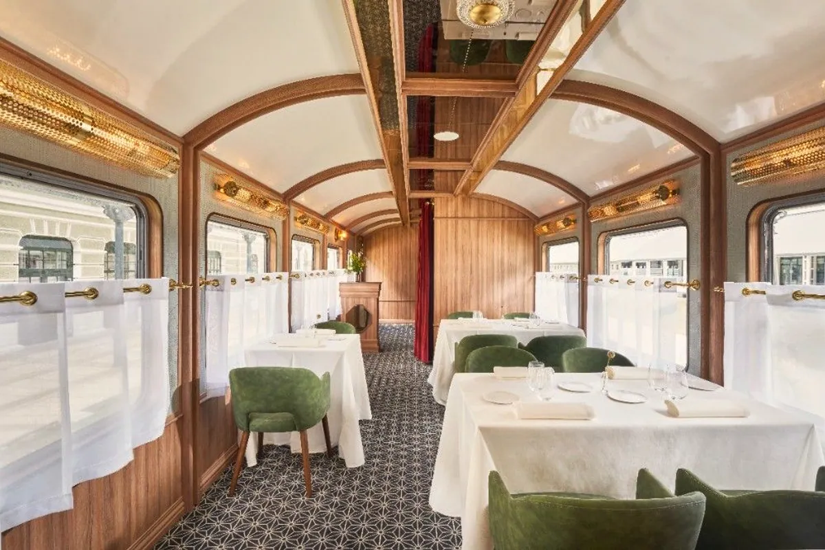 Comedor dentro de un vagón de tren rehabilitado con sillas verdes y mesas vestidas
