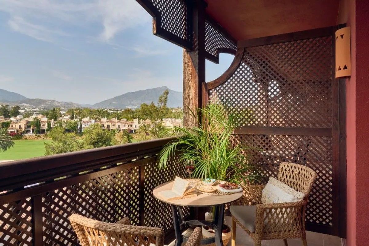 Balcón de habitación con mesa, sillas de mimbre y vistas al golf y la montaña