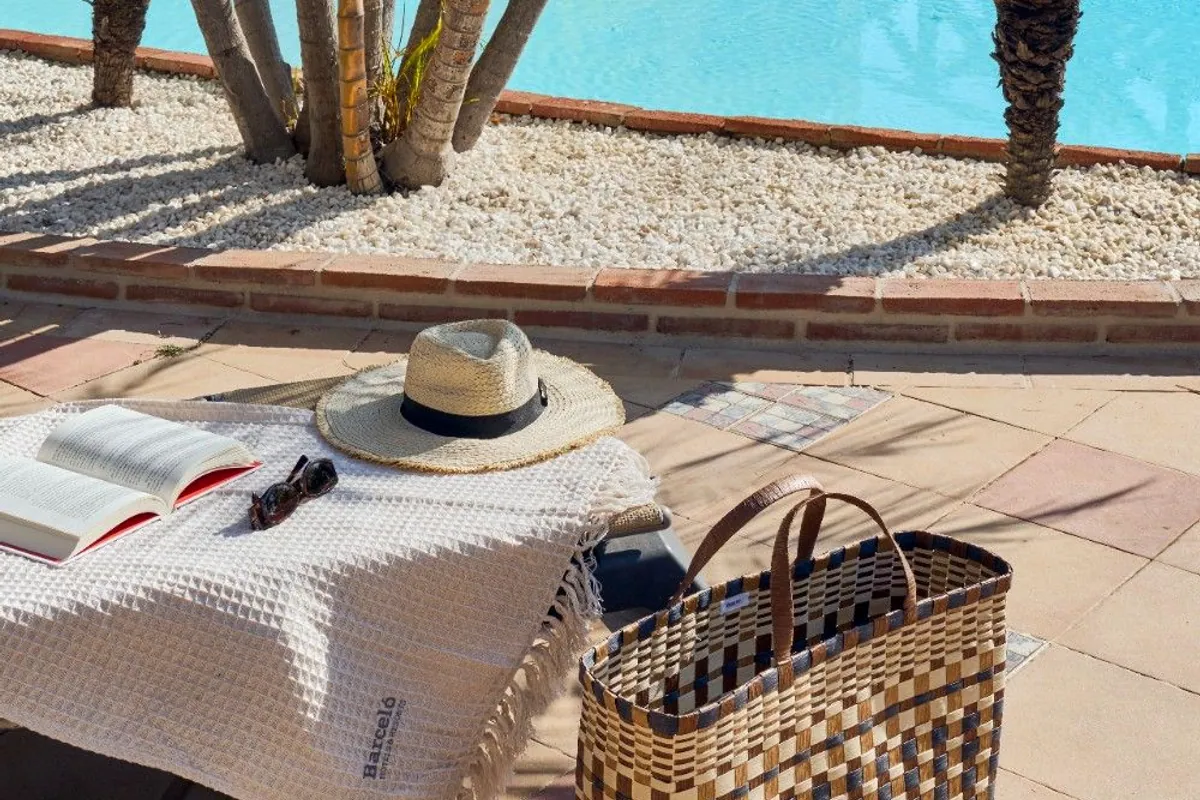 Piscina del hotel con palmeras, hamaca con toalla, sombrero de paja y capazo