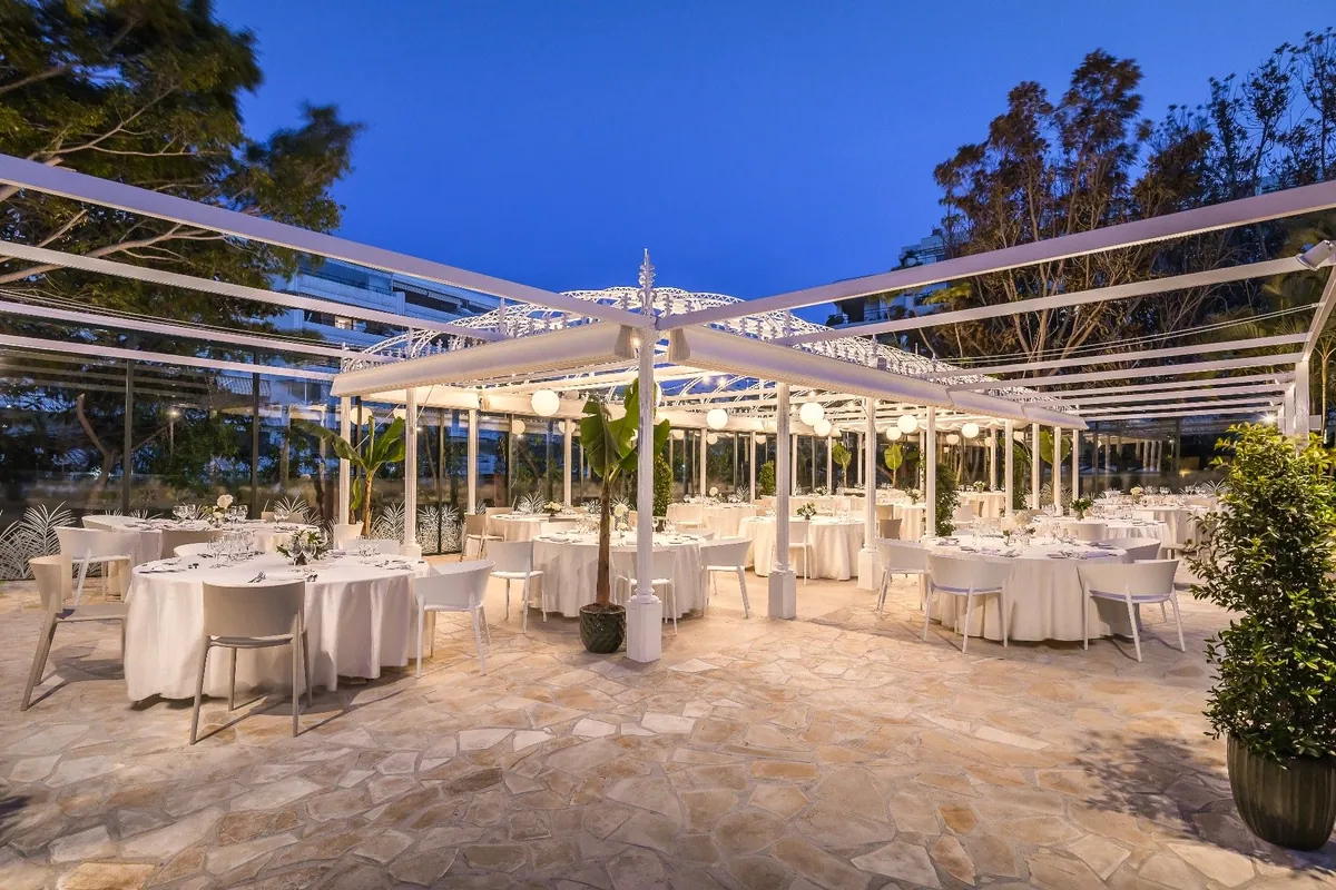 Mesas montadas bajo la pérgola blanca de La Carpa del Barceló Marbella al anochecer