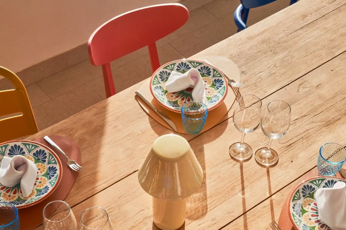 Mesa de madera puesta con vajilla de colores, copas y lámpara en un hotel