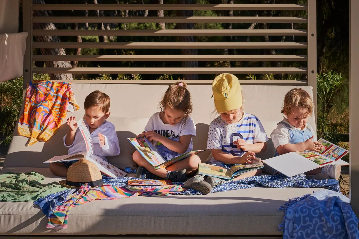 Cuatro niños sentados en un sofá exterior del resort leyendo cuentos