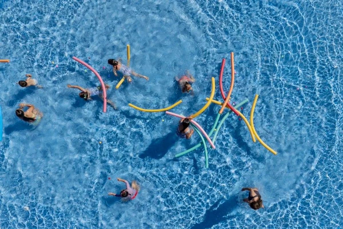 Vista aérea de la piscina del resort con niños jugando con churros de colores