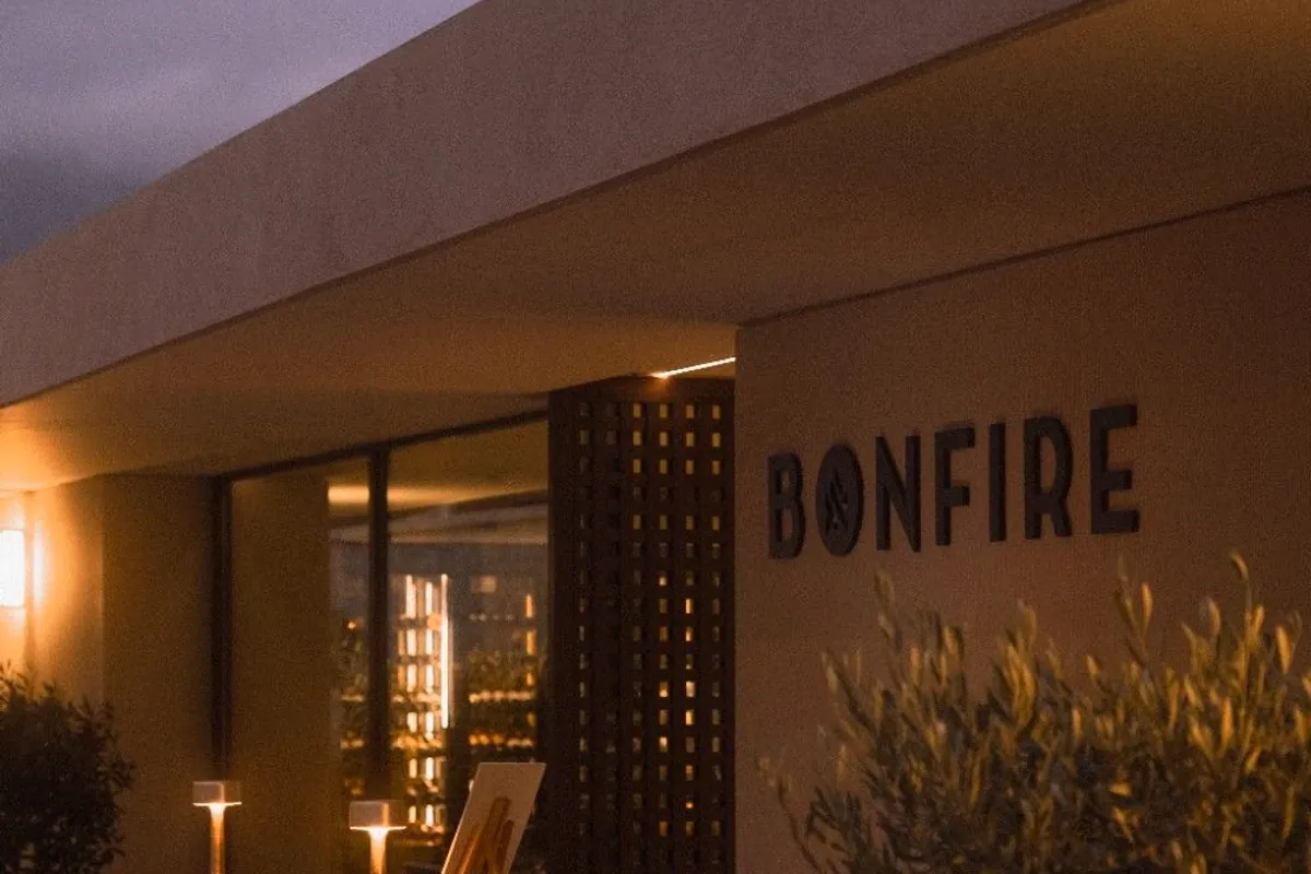 Entrada del restaurante Bonfire iluminada al anochecer con un olivo en primer plano