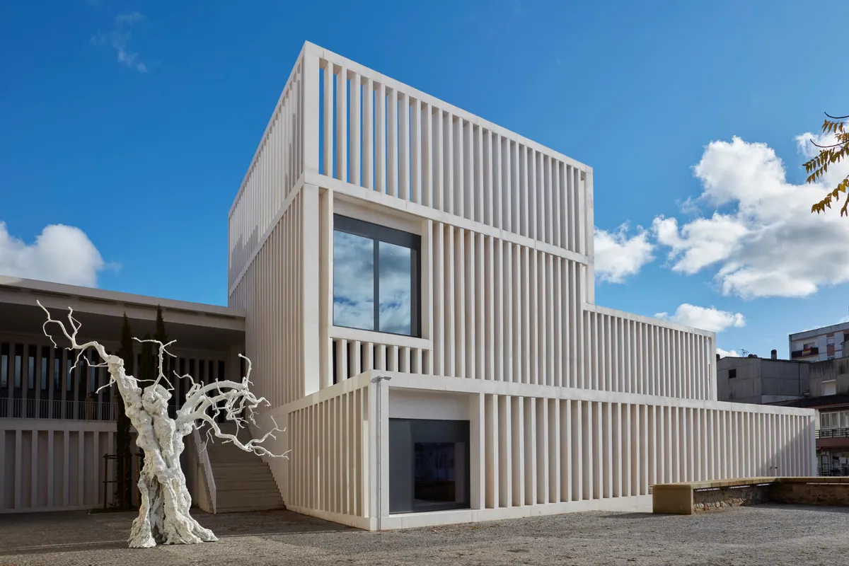 Fachada blanca del Museo Helga de Alvear en Cáceres con escultura de árbol