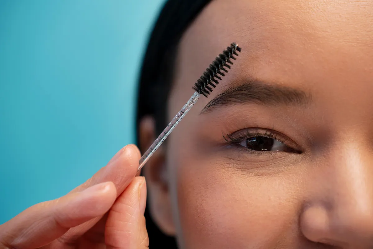 Mujer peinándose las cejas con un cepillo de maquillaje