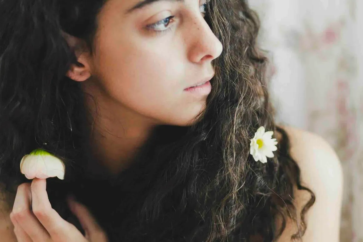 Mujer de pelo largo y rizado con una flor blanca prendida en el cabello
