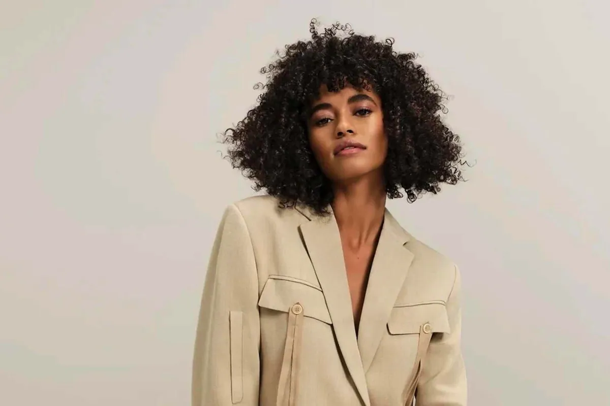 Mujer con melena rizada voluminosa y flequillo rizado, con americana beige