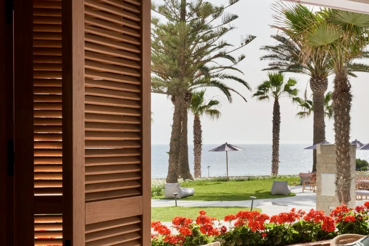 Mesa junto a una ventana con vistas a palmeras, flores rojas y el mar en Conil