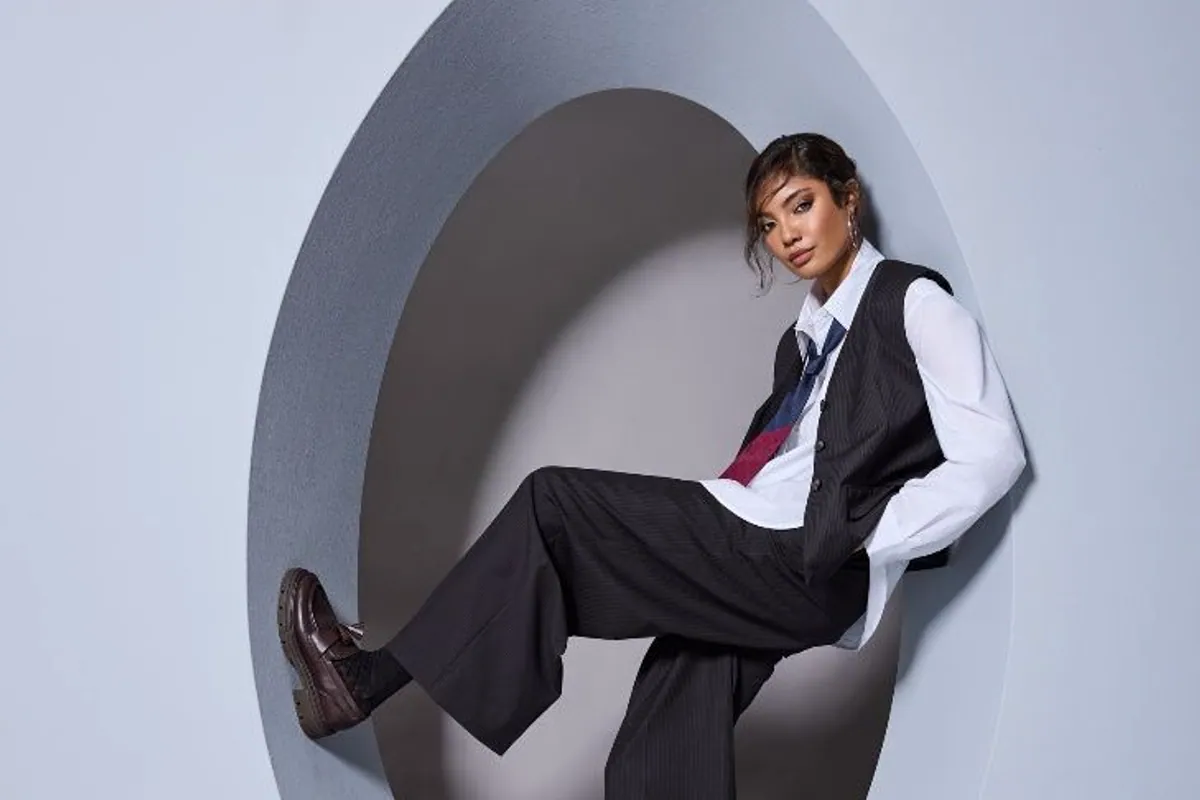 Modelo con chaleco y pantalón negro apoyada en un círculo, con mocasines marrones