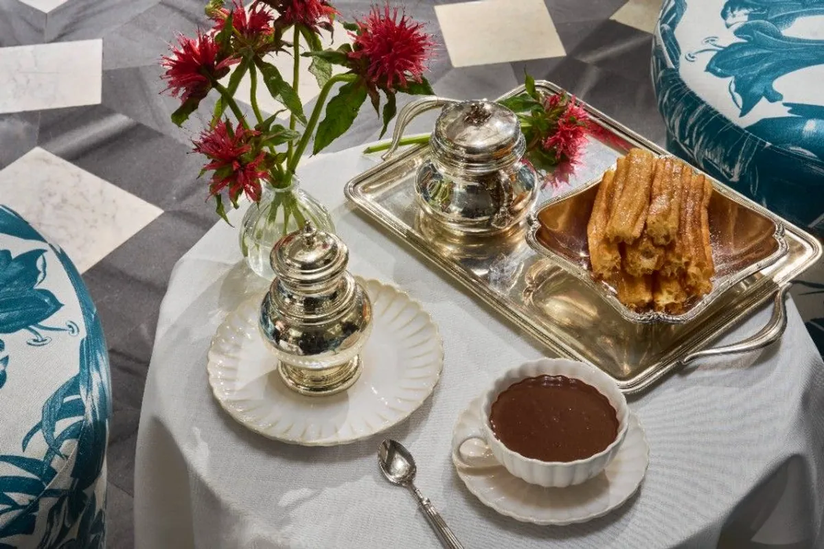 Bandeja de plata con churros y taza de chocolate caliente en una mesa