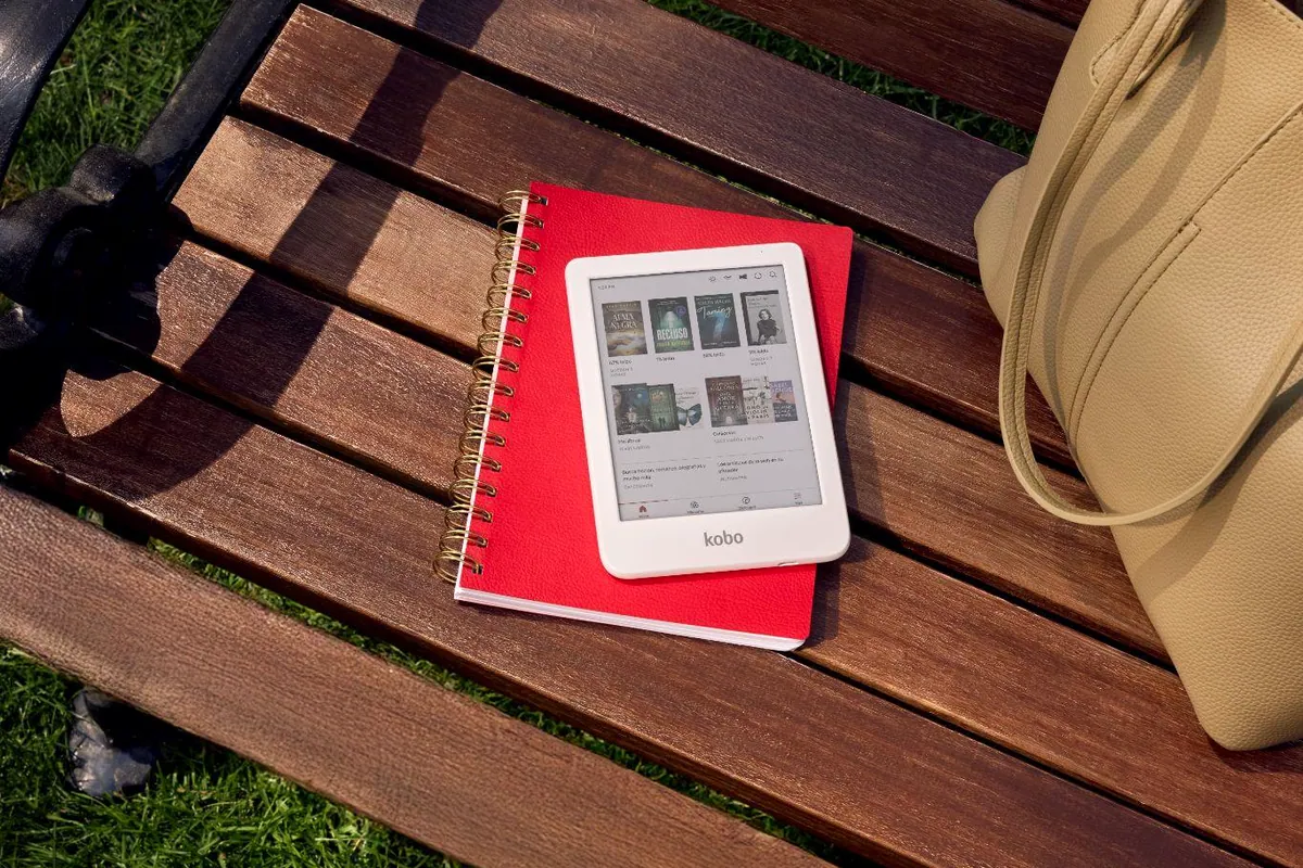 eReader Kobo sobre un cuaderno rojo en un banco de parque, junto a un bolso