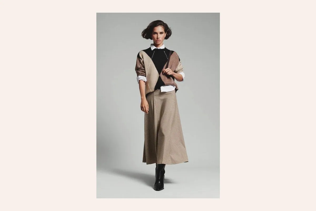 Look preppy de Lefties con jersey de pico, camisa blanca y falda de tablas