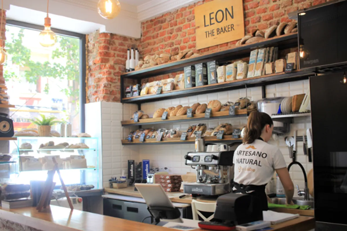 Interior de una tienda Leon the Baker con panes en las estanterías y una empleada tras el mostrador