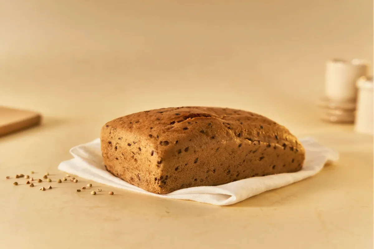 Hogaza de pan de trigo sarraceno germinado sobre un paño blanco con semillas al lado