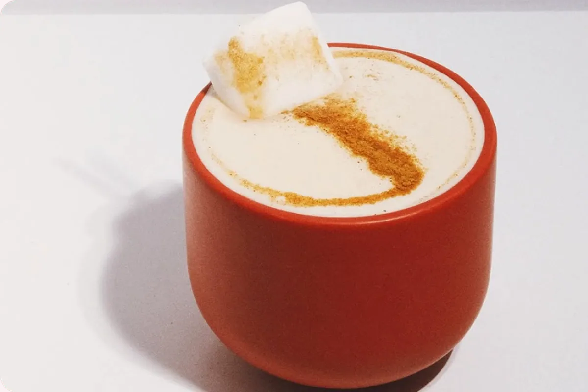 Taza naranja con un café con leche espumoso y canela por encima