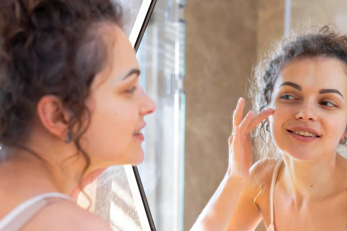 Mujer aplicándose crema hidratante frente al espejo