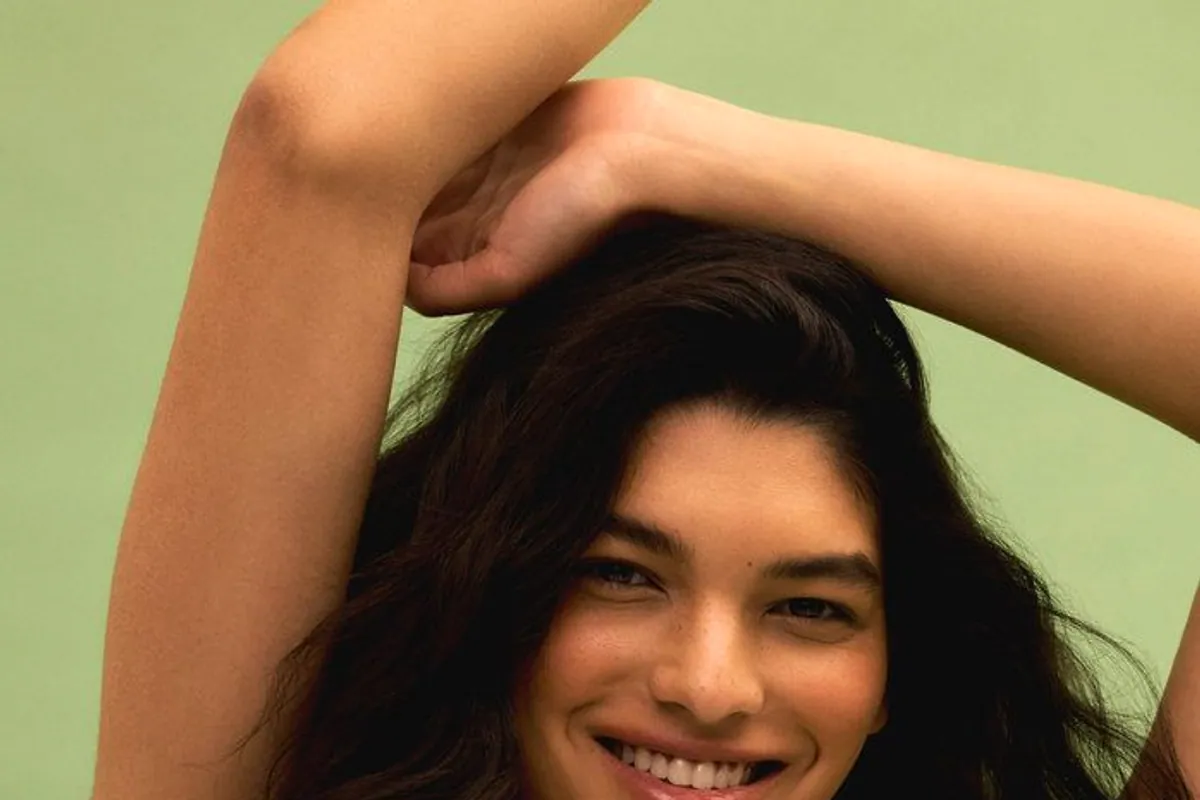 Mujer morena sonriendo con los brazos sobre la cabeza y fondo verde