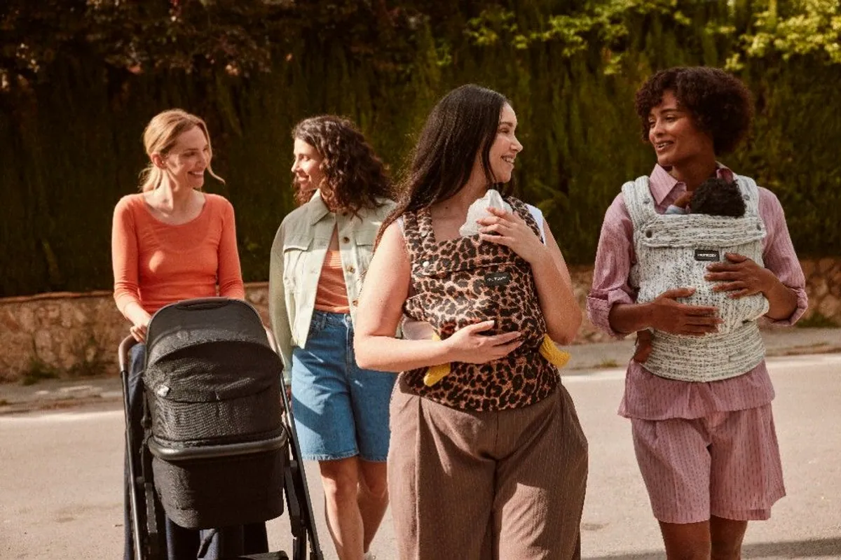 Cuatro madres paseando por la calle con un carrito y dos bebés en mochila portabebés