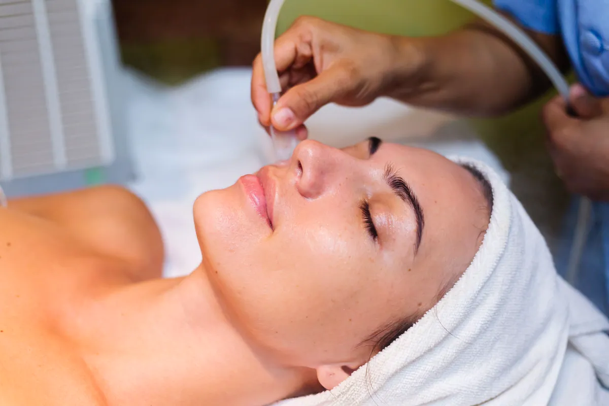 Mujer tumbada en la camilla de una clinica estetica durante un tratamiento facial