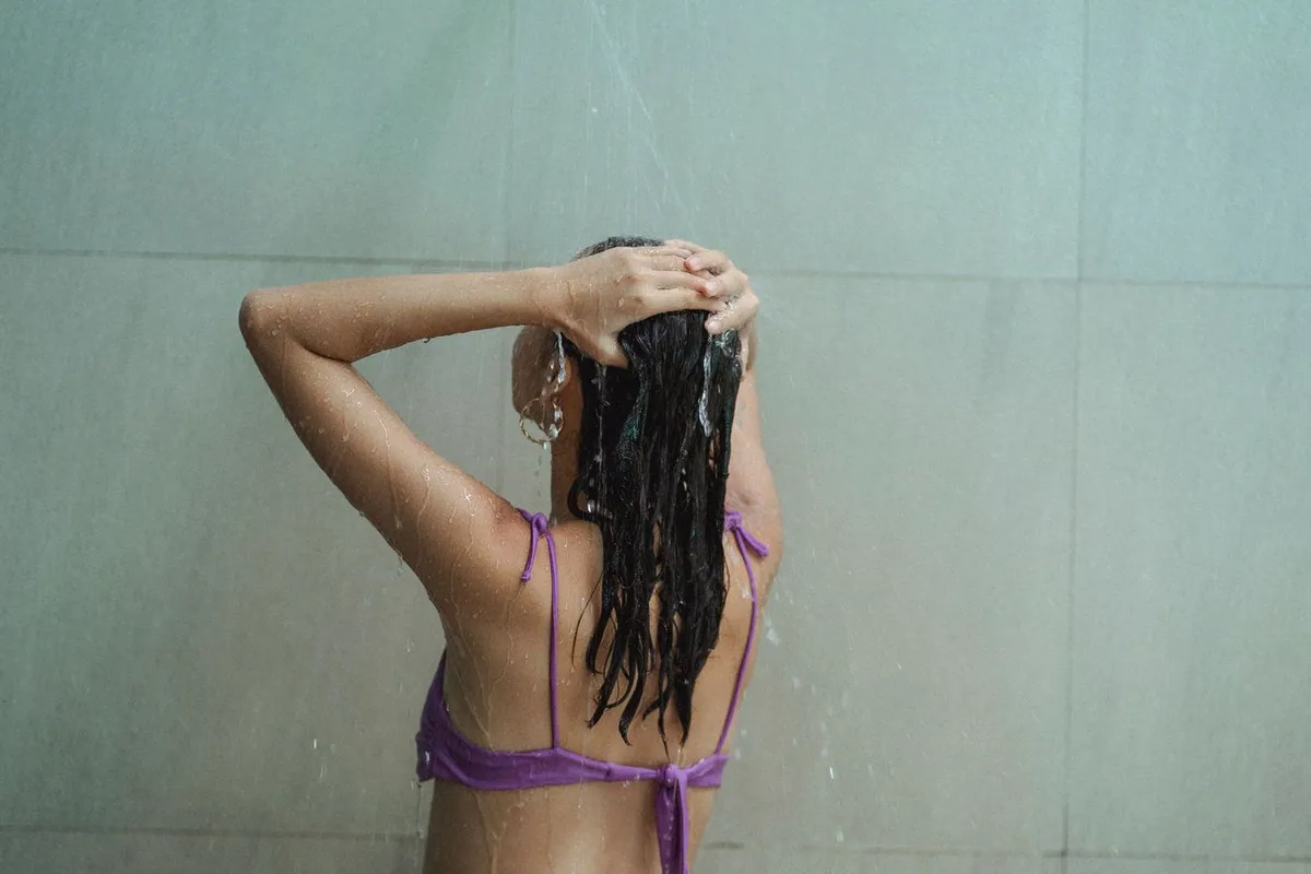 Mujer de espaldas en la ducha pasándose la mano por el pelo mojado