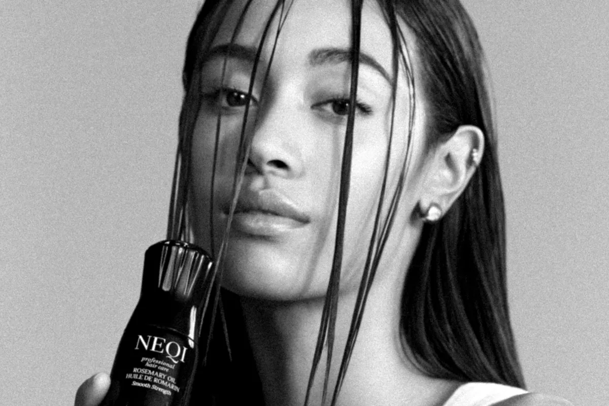 Modelo con el pelo mojado sujetando el frasco del aceite de romero de NEQI