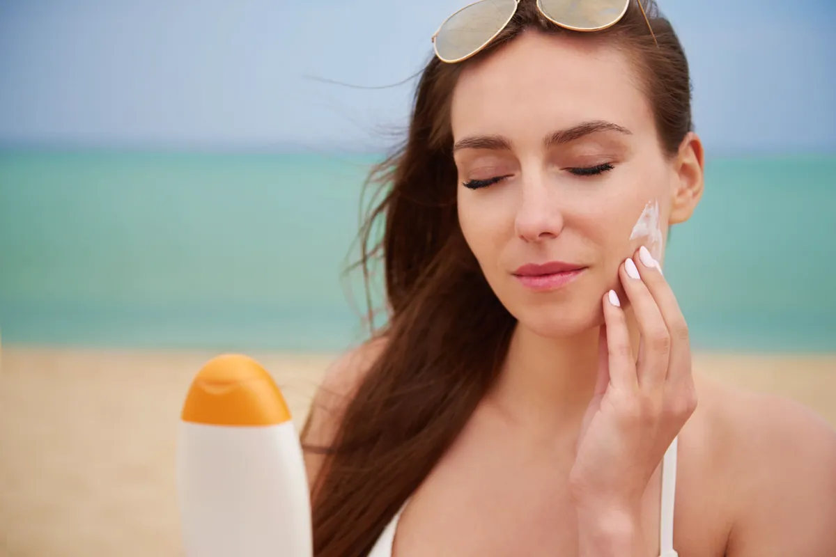 Mujer aplicándose crema solar en la cara en la playa