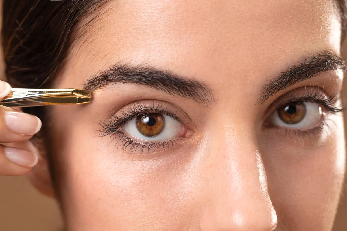Mujer cuidándose las cejas en casa frente al espejo