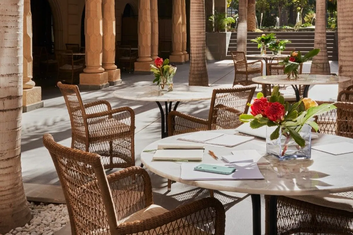 Terraza del hotel Santa Catalina con columnas, palmeras y mesas redondas montadas