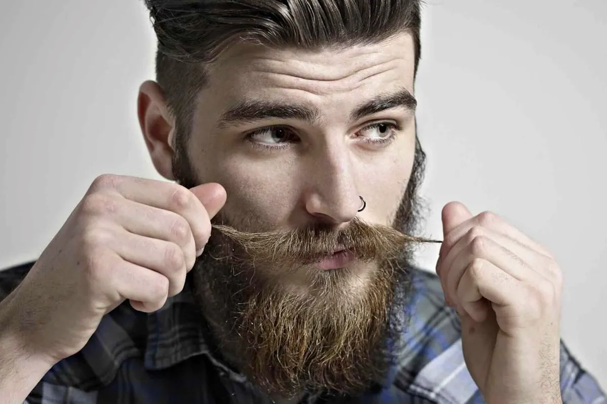 Hombre joven con barba y bigote retorciéndose las puntas del bigote con las manos