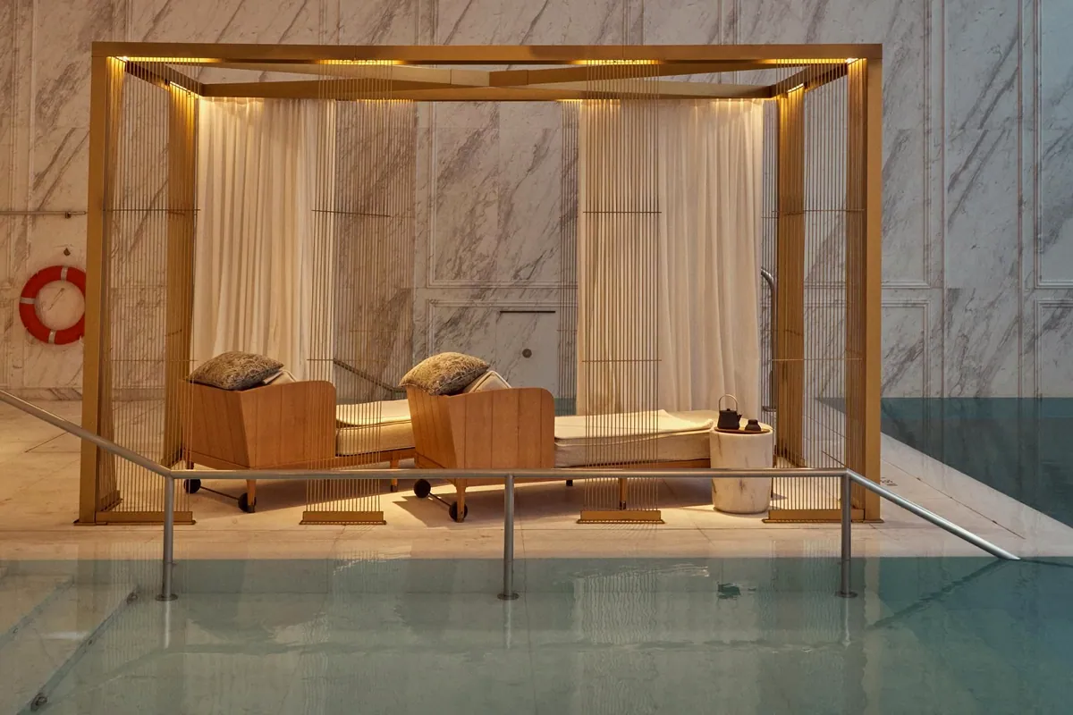Piscina interior de mármol con camas y dosel dorado en el spa del hotel