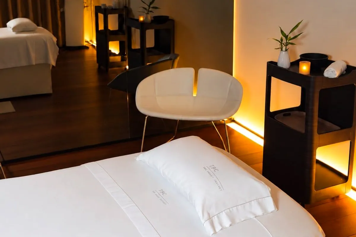 Cabina blanca con camilla, lámparas doradas y butaca en el spa de Barcelona