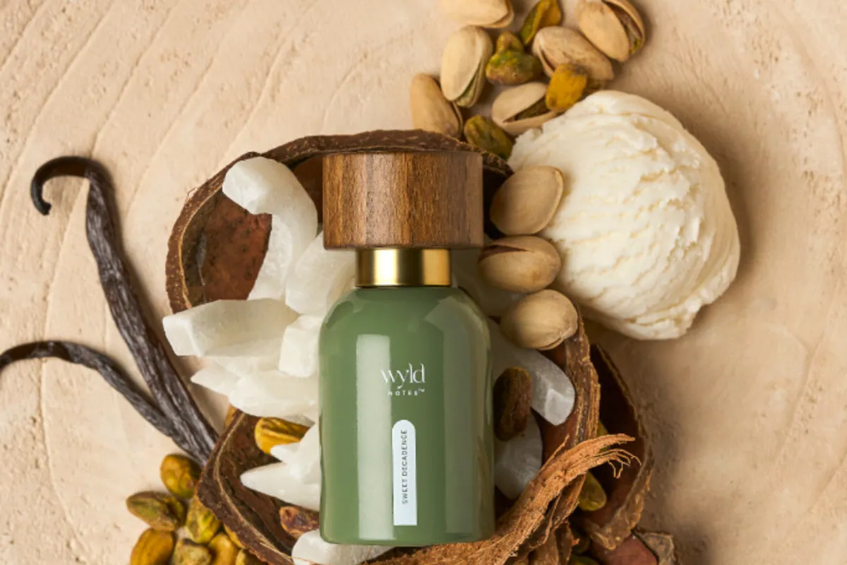 Frasco verde de perfume Sweet Decadence de Wyld Notes rodeado de pistachos, coco y vainilla