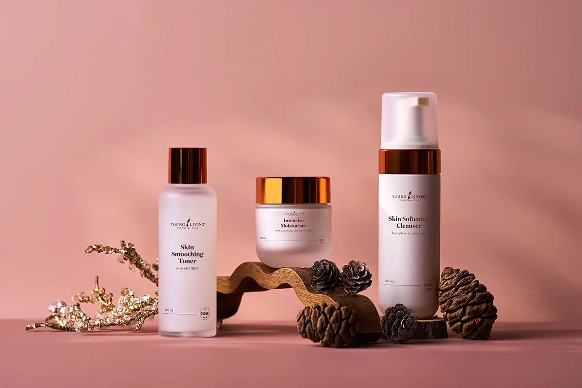 Tónico, crema hidratante y limpiador de la nueva línea facial de Young Living sobre fondo rosa